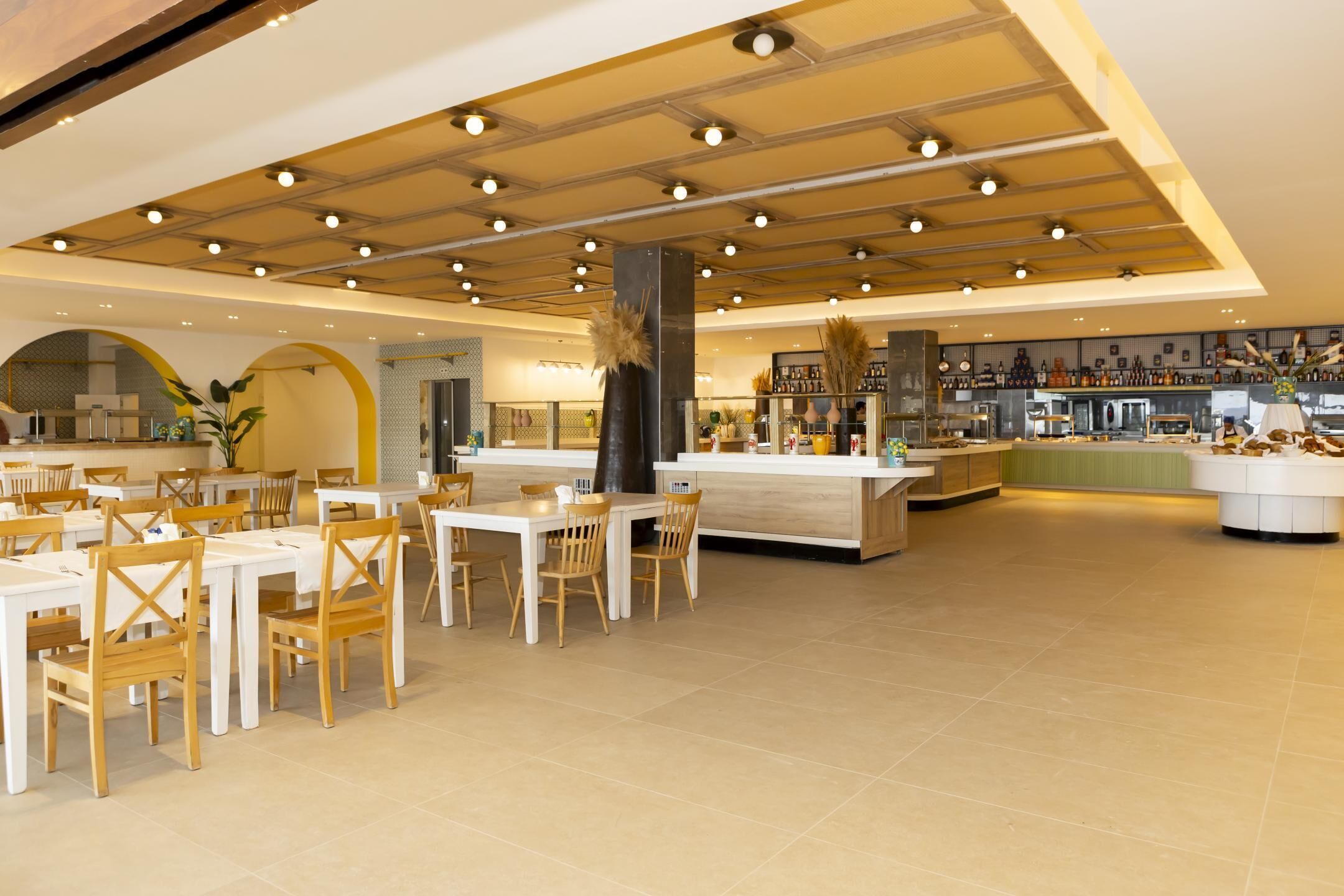 A spacious dining area with multiple tables and chairs, a central bar area with a counter, and a kitchen visible in the background.