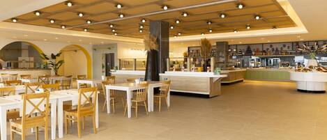 A spacious dining area with multiple tables and chairs, a central bar area with a counter, and a kitchen visible in the background.