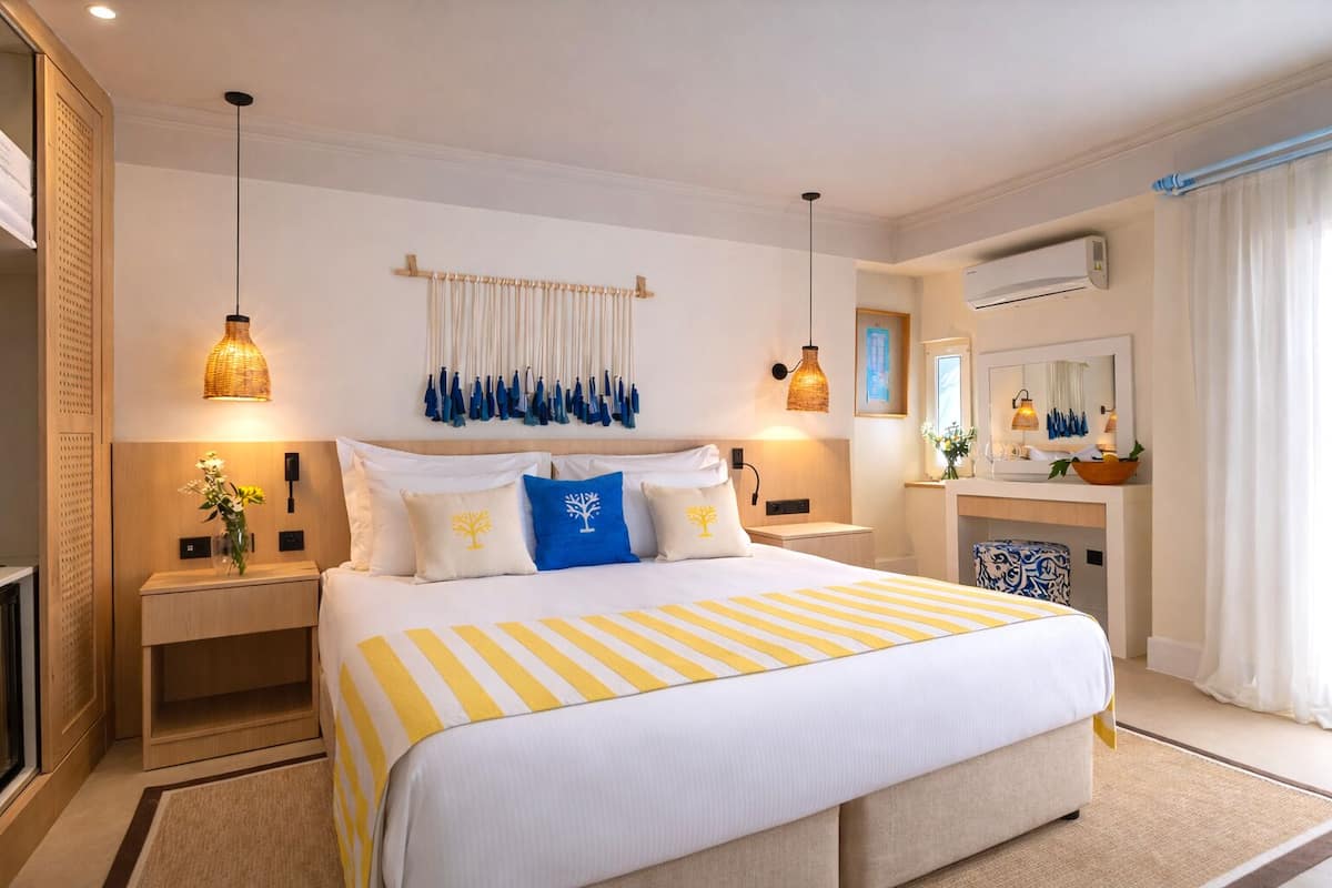Habitación de hotel con una cama grande, mesitas de noche, un espejo, aire acondicionado y una ventana con cortinas.