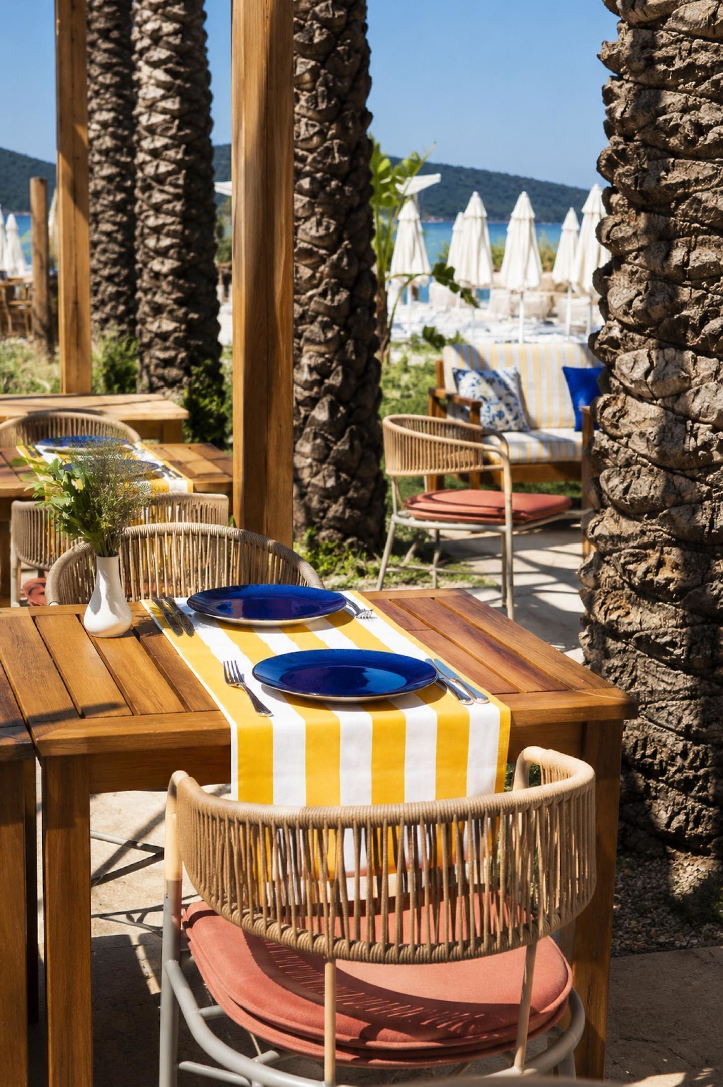 Outdoor dining tables with chairs, a view of the beach, and umbrellas in the background.