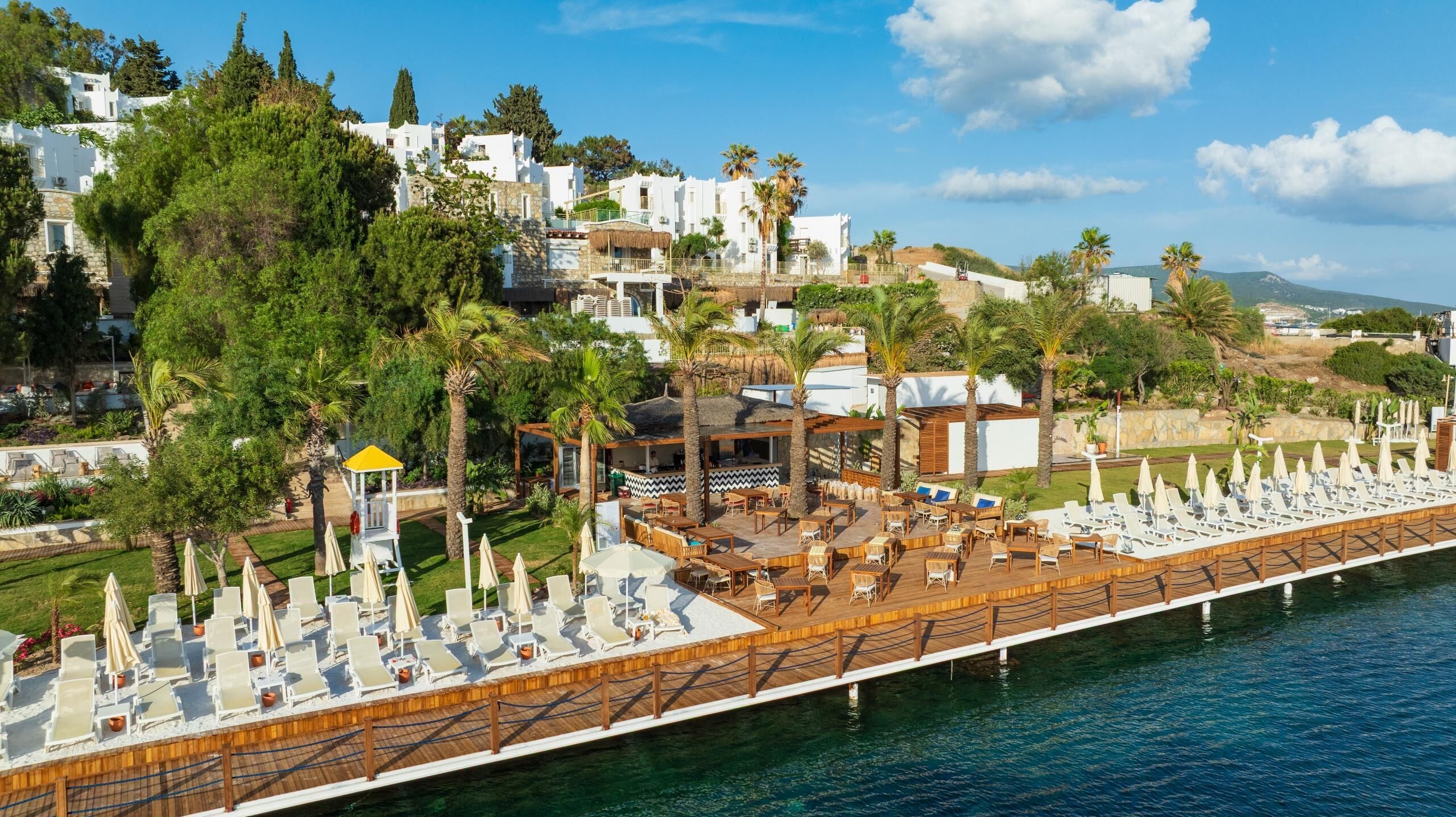 Un resort con zona de piscina, sillones de descanso y vista al mar.