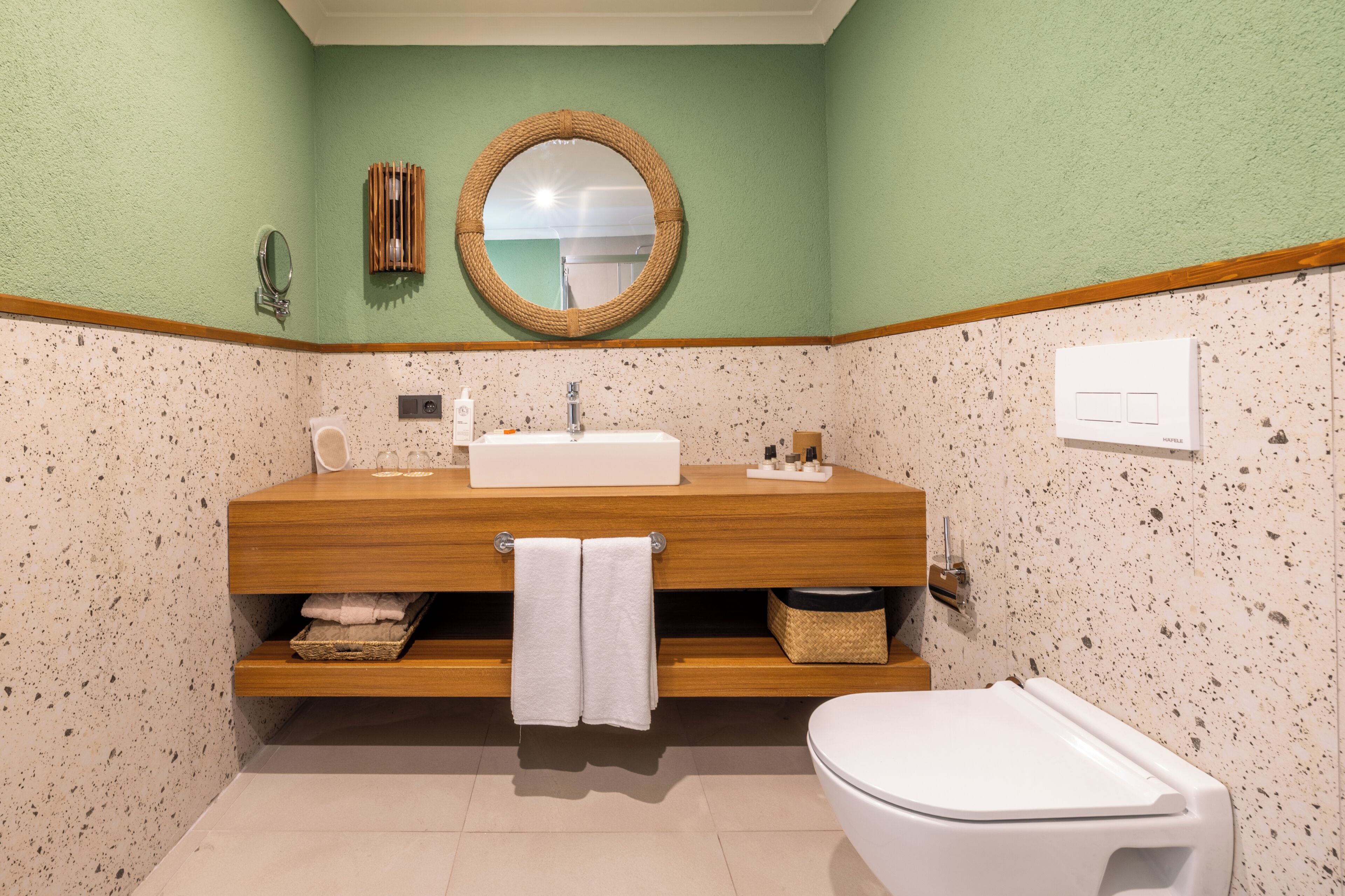 Een badkamer met een houten wastafelmeubel, een ronde spiegel, een toilet en een wasbak.