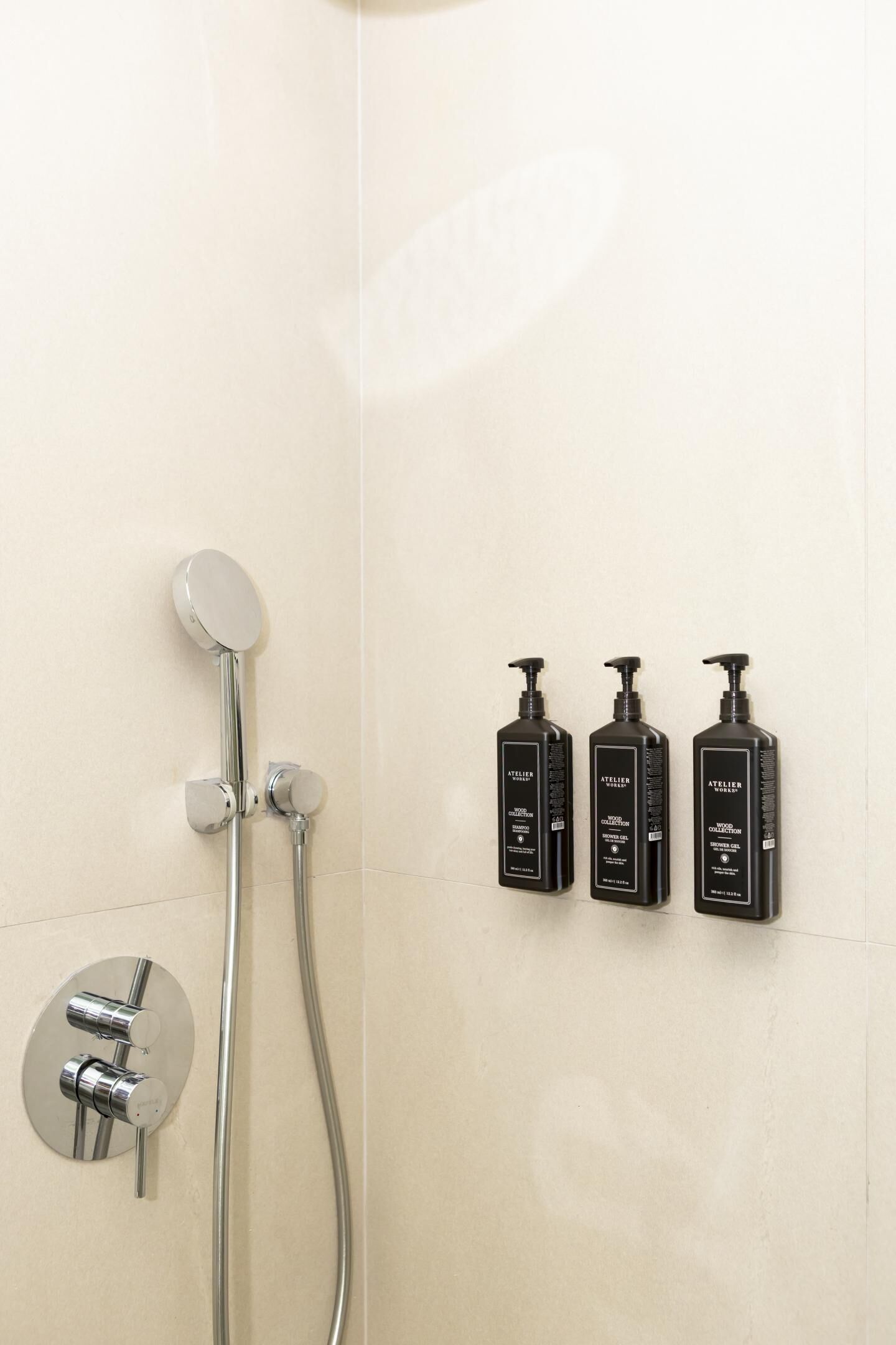 Een douchegedeelte met een handdouche, een wandmengkraan en drie zwarte toiletartikelen.