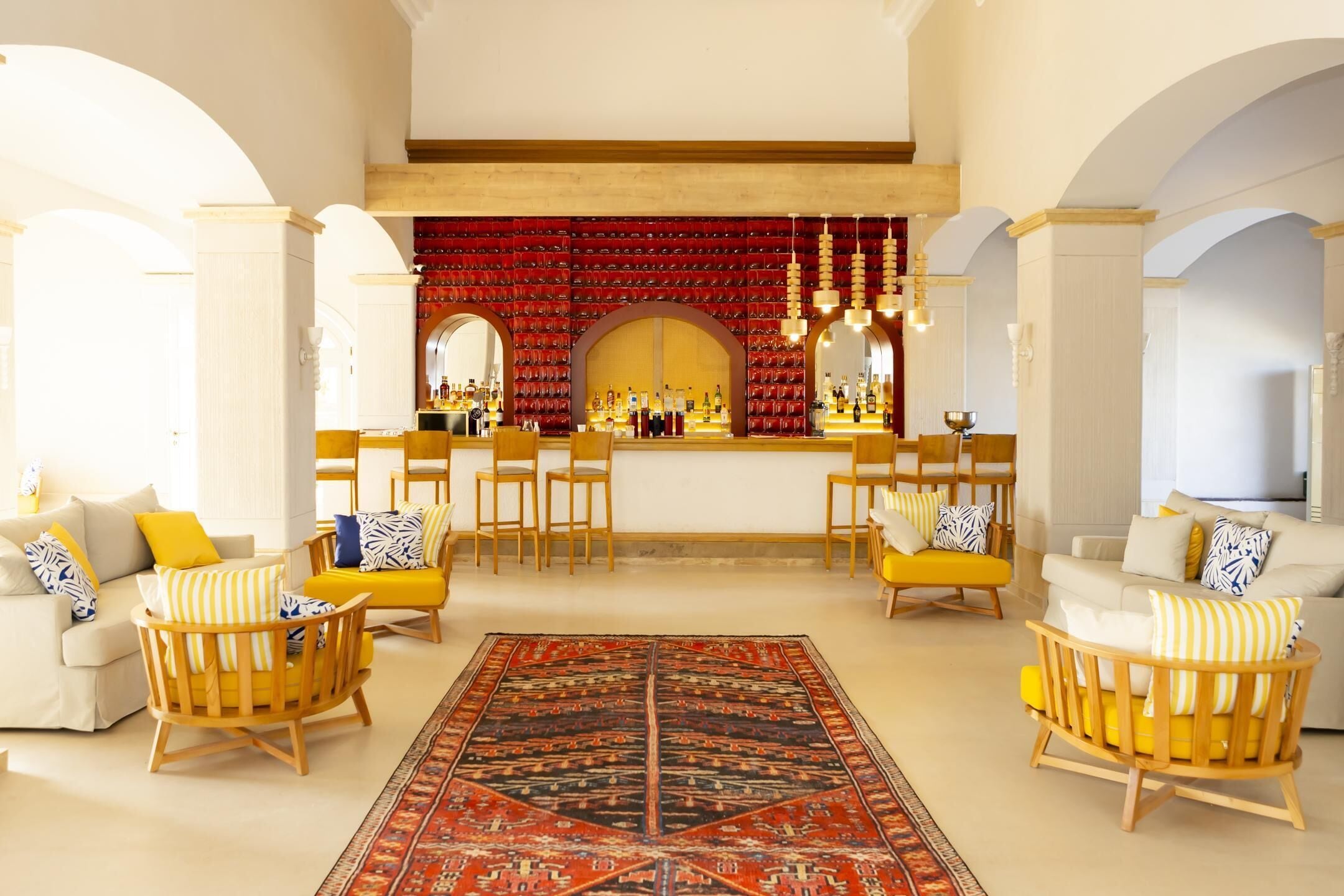 Amplia sala de estar con barra, sillones amarillos y alfombra estampada.