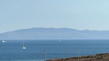 Escena costera con varios veleros anclados en aguas tranquilas, cielo despejado y montañas a lo lejos.
