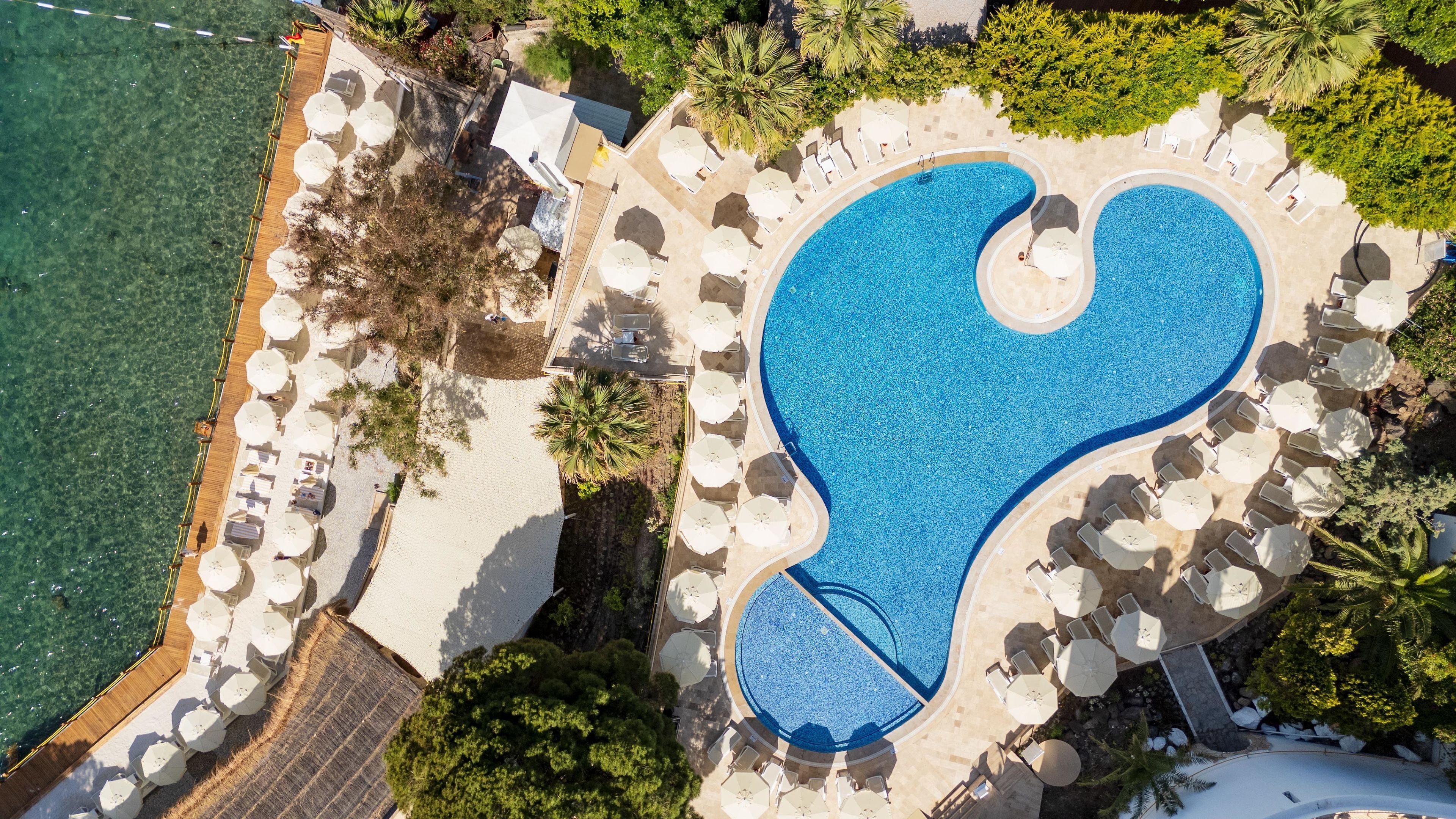 An aerial view of a resort with a large pool, sun loungers, and a wooden deck.