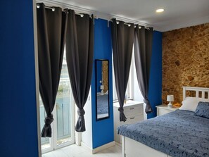 A bedroom with a bed, a nightstand, a mirror, and a window with curtains. - Modern Apartment in Lisbon (Lisboa)