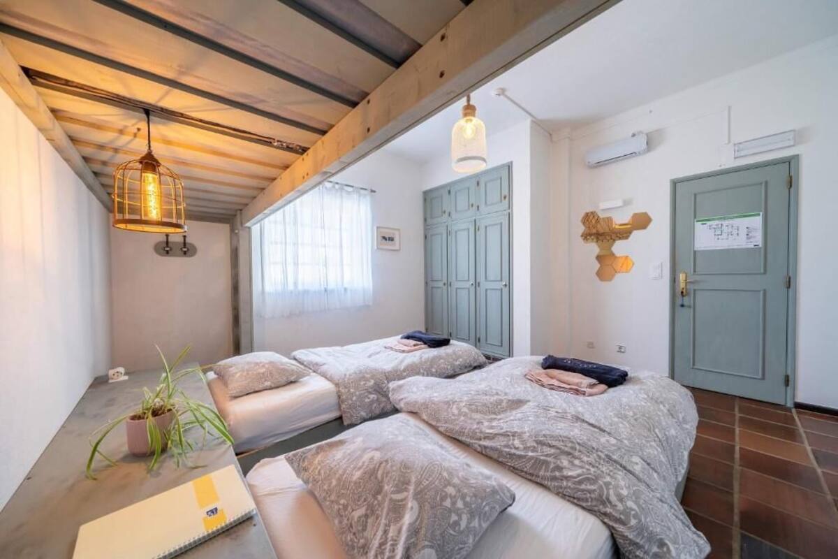 Una habitación con dos camas, una planta en maceta, un cuaderno y una lámpara colgante.