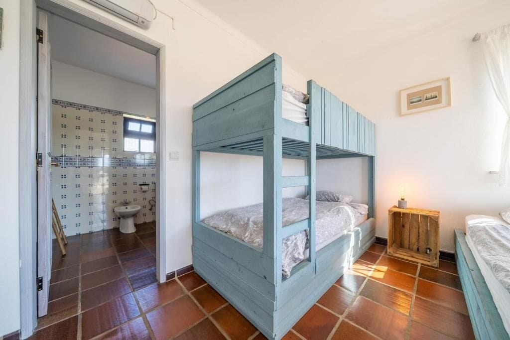 A room with a bunk bed, a small wooden cabinet, and a bathroom with a toilet and patterned tiles.