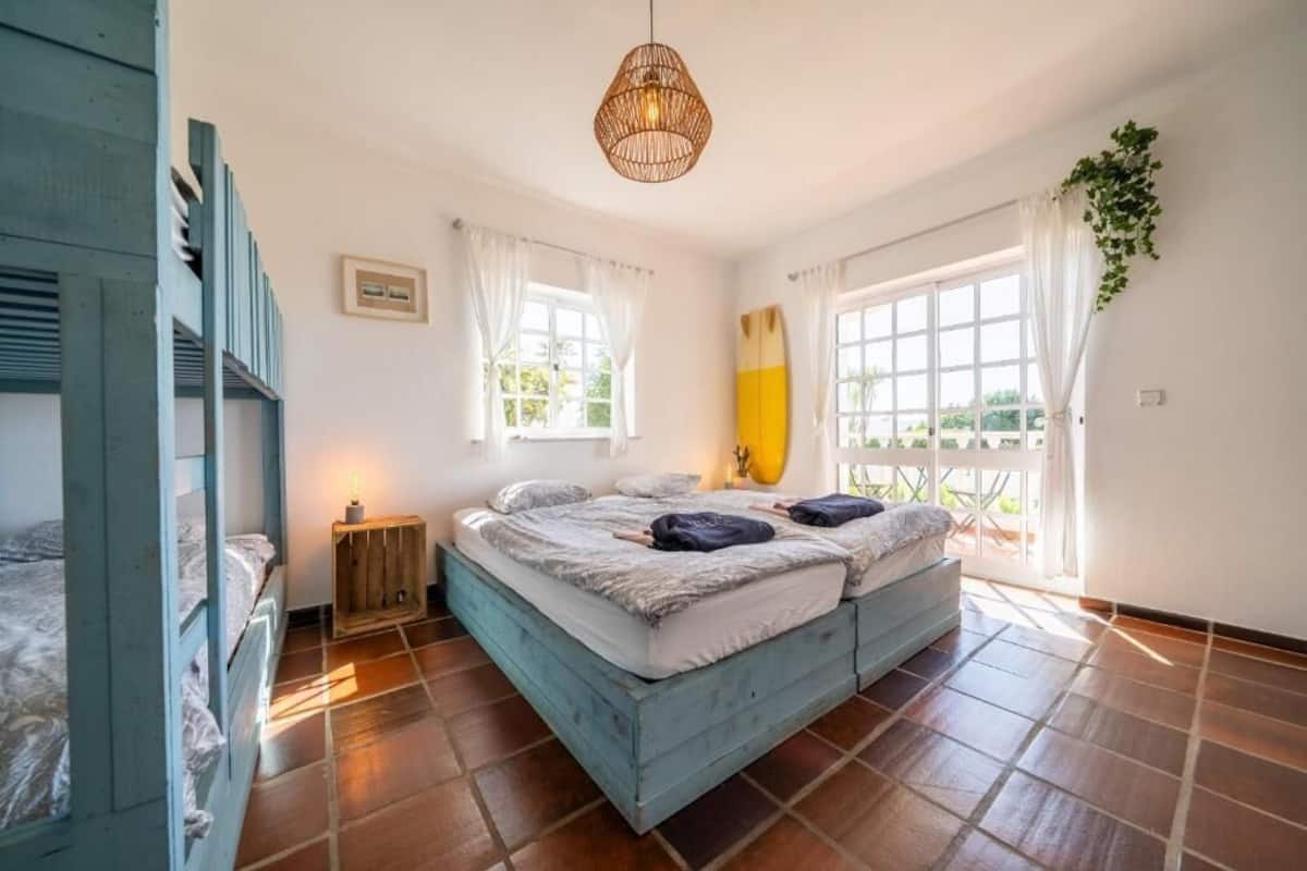 Un dormitorio con cama, mesita de noche, lámpara colgante y ventana con cortinas.