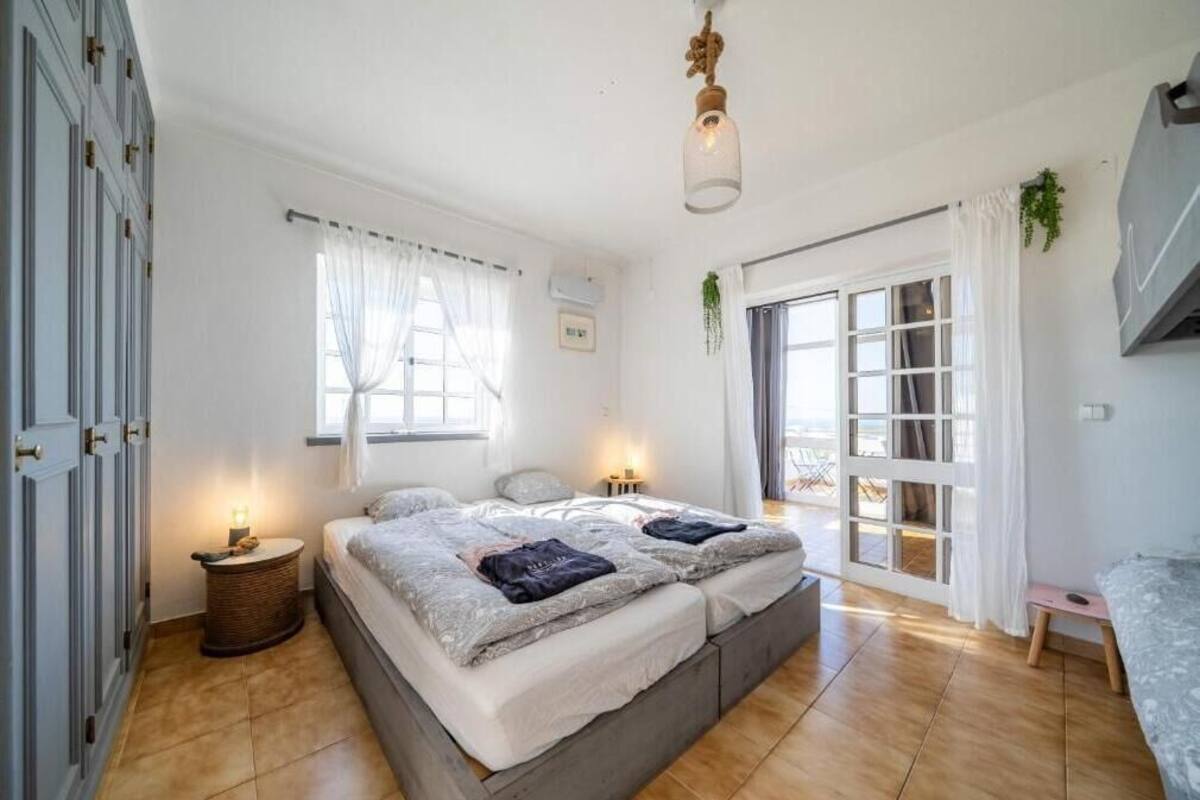 Un dormitorio con una cama grande, dos mesitas de noche, una planta colgante y un ventanal corredero al exterior.