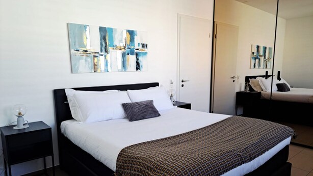 A bedroom with a bed, nightstands, a bedside table, and abstract wall art. - Just steps away from Parco Ciani (Mola Mimosa) (Lugano)