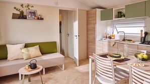Un espacio habitable compacto con sofá, una mesa de comedor con sillas, una zona de cocina y una pequeña mesita con hervidor.