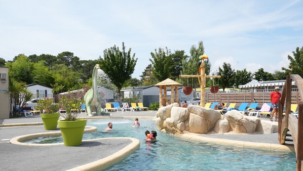 Un área de piscina con tobogán de agua, sillas de descanso y un pabellón.