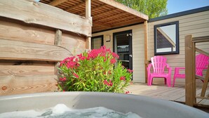 Una terraza de madera con un jacuzzi, sillas rosas y un arbusto de flores.