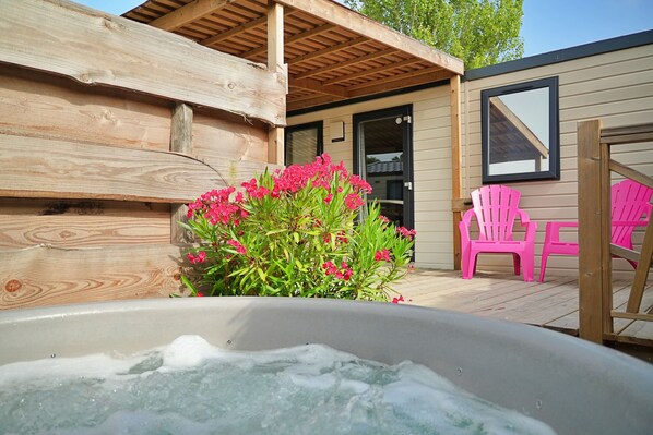 Una terraza de madera con un jacuzzi, sillas rosas y un arbusto de flores.