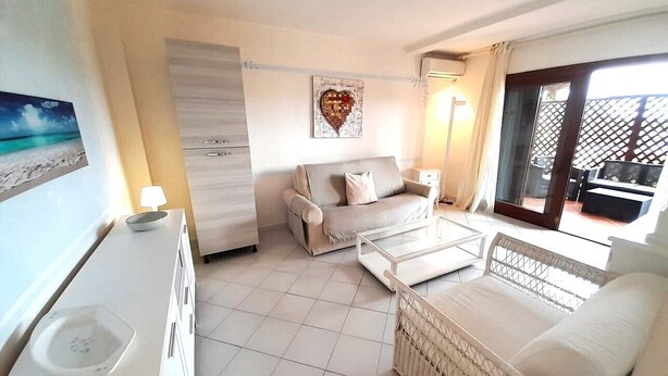 A modern, well-lit room with a sofa, a small table, and a wicker chair. - ELEGANTE BILO D2 CASA SANDRA (Golfo di Marinella)