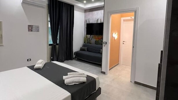 Ein modernes Hotelzimmer mit Bett, Sofa, Flachbildfernseher und einer Tür zum Badezimmer.