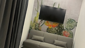 Ein modernes Wohnzimmer mit einem grauen Sofa, einem flachbildfernseher an einer strukturierten Wand und einer Deckenleuchte.