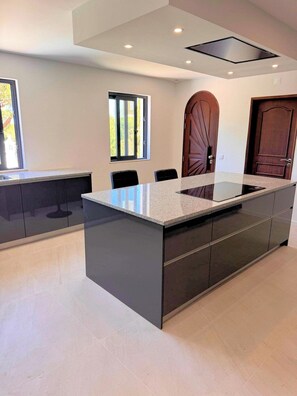 A modern kitchen with a central island, recessed ceiling lights, and a large window. - Casa Vilamoura Luxe | Luxury 9BR retreat | Walk to Marina | Vilamoura (Quarteira)