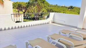 Un área de estar al aire libre con sillones de sol y vistas a árboles y edificios.