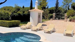 Una piscina con sillas de descanso, un pequeño edificio blanco y una puerta.