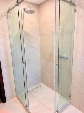 Eine Duschkabine mit Glaswänden, einer Handbrause, einer Glastür und einem gefliesten Boden.