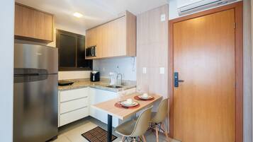 A compact kitchen with a stainless steel refrigerator, a microwave, and a sink. There is a dining table with two chairs and a small rug.