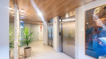 A modern hallway with elevators, a large abstract painting, and a potted plant.