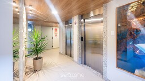 A modern hallway with elevators, a large abstract painting, and a potted plant. - Studio in Condo w/ Pool and Gym Ftw1106 (Salvador)