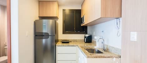 Una cocina compacta con refrigerador de acero inoxidable, microondas, cafetera y pileta.