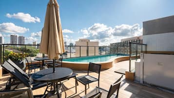A rooftop pool area with lounge chairs, a table, and an umbrella.