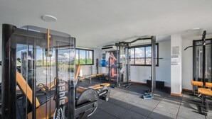 A gym with exercise equipment, benches, and a view of a cityscape through large windows. - Studio in Condo w/ Pool and Gym Ftw1106 (Salvador)