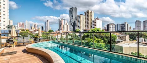 A rooftop pool with a city skyline view, wooden deck, and outdoor seating area.