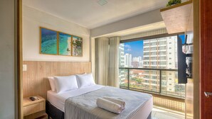 A hotel room with a bed, a nightstand, a window with a city view, and artwork on the wall. - Studio in Condo w/ Pool and Gym Ftw1106 (Salvador)