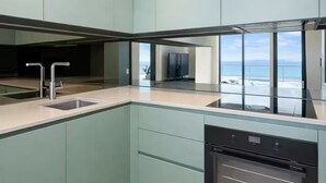 Cozinha moderna com forno embutido, pia e vista para o oceano.