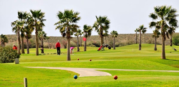 Un campo de golf con palmeras, cielo despejado y algunas personas jugando.