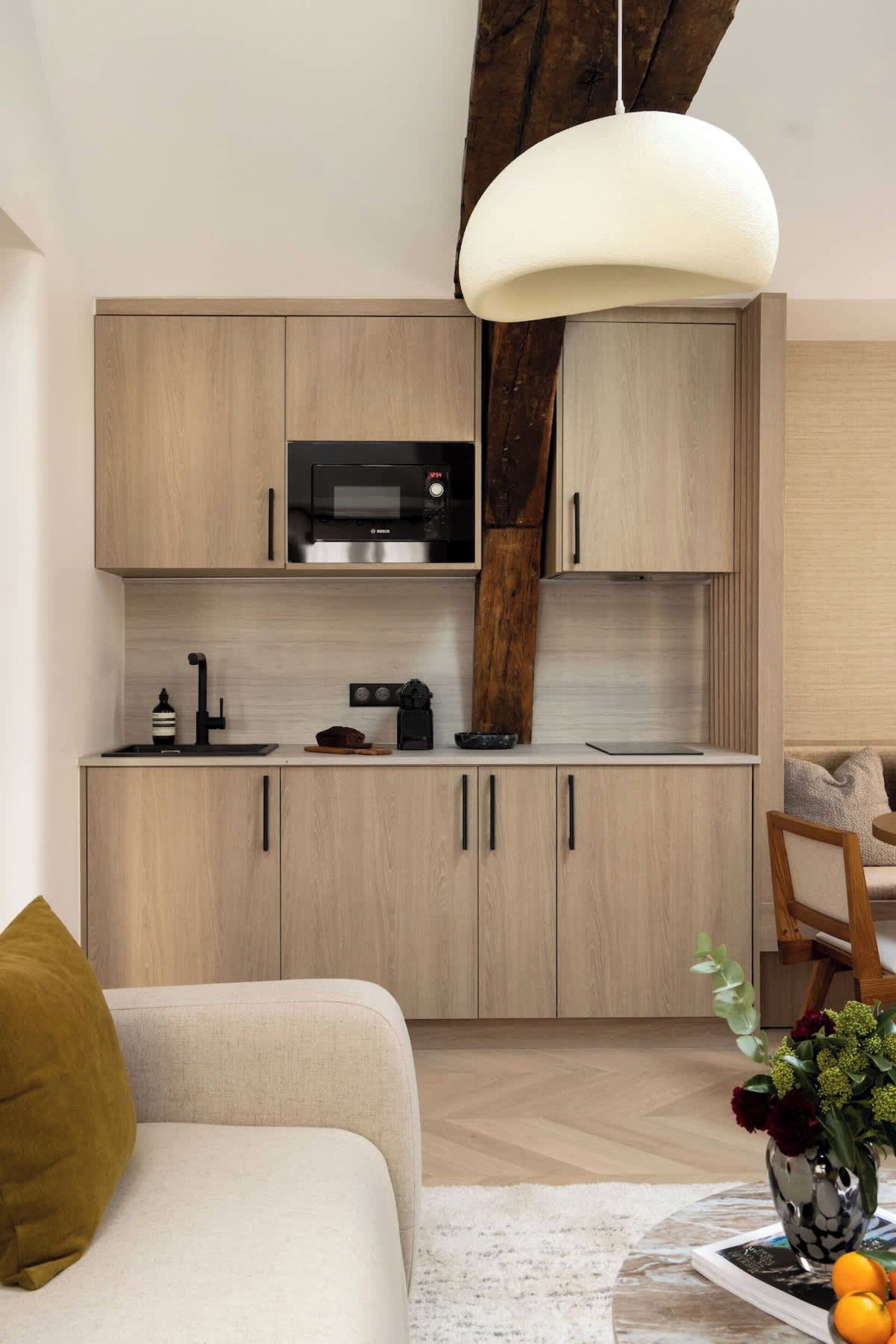 Une cuisine moderne avec des meubles de couleur bois clair, un micro-ondes noir et un luminaire suspendu.
