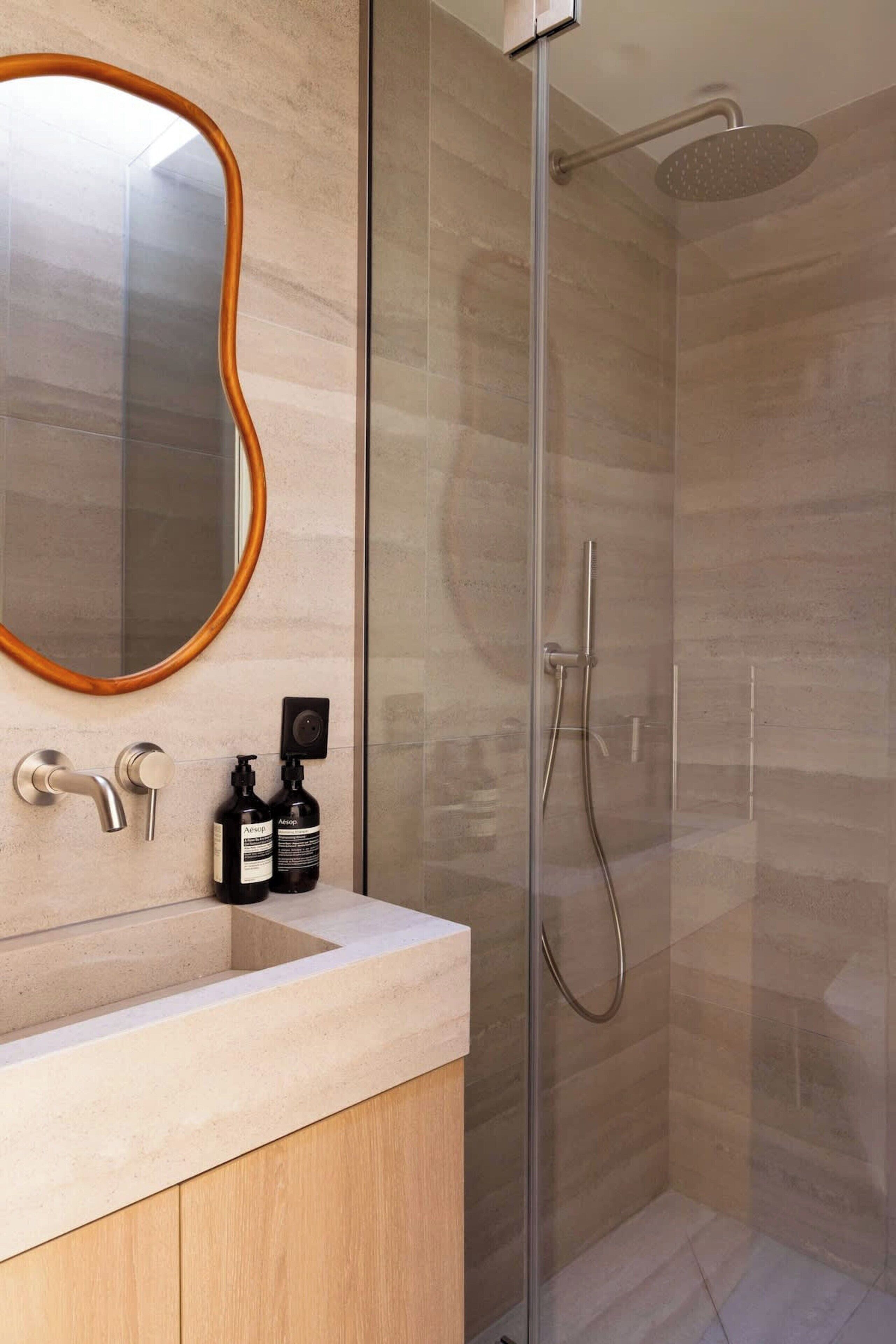 A modern bathroom with a glass-enclosed shower, a wooden-framed mirror, and a minimalist sink area.