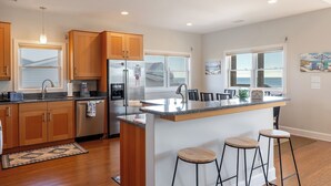 Una cucina moderna con mobili in legno, elettrodomestici in acciaio inossidabile, una grande isola con sgabelli da bar e ampie finestre che si affacciano sull'oceano.