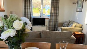 Une table à manger est dressée avec des assiettes, des couverts et des verres à vin, et un vase de fleurs est placé sur le côté gauche.