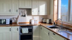 Une cuisine moderne avec des armoires blanches, un plan de travail en bois, un four encastré, un évier et une fenêtre qui laisse entrer la lumière naturelle.