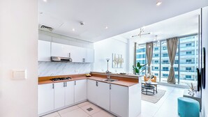 A modern kitchen with white cabinets, a marble countertop, and a gas stove. There is a dining area with a table and chairs, and a large window offering a view of a building. - Marina View Stay with Rooftop Pool (Dubai)