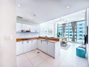 Eine moderne Küche mit weißen Schränken, einer Marmorarbeitsplatte und einem Gasherd. Es gibt einen Essbereich mit Tisch und Stühlen sowie ein großes Fenster mit Blick auf ein Gebäude.