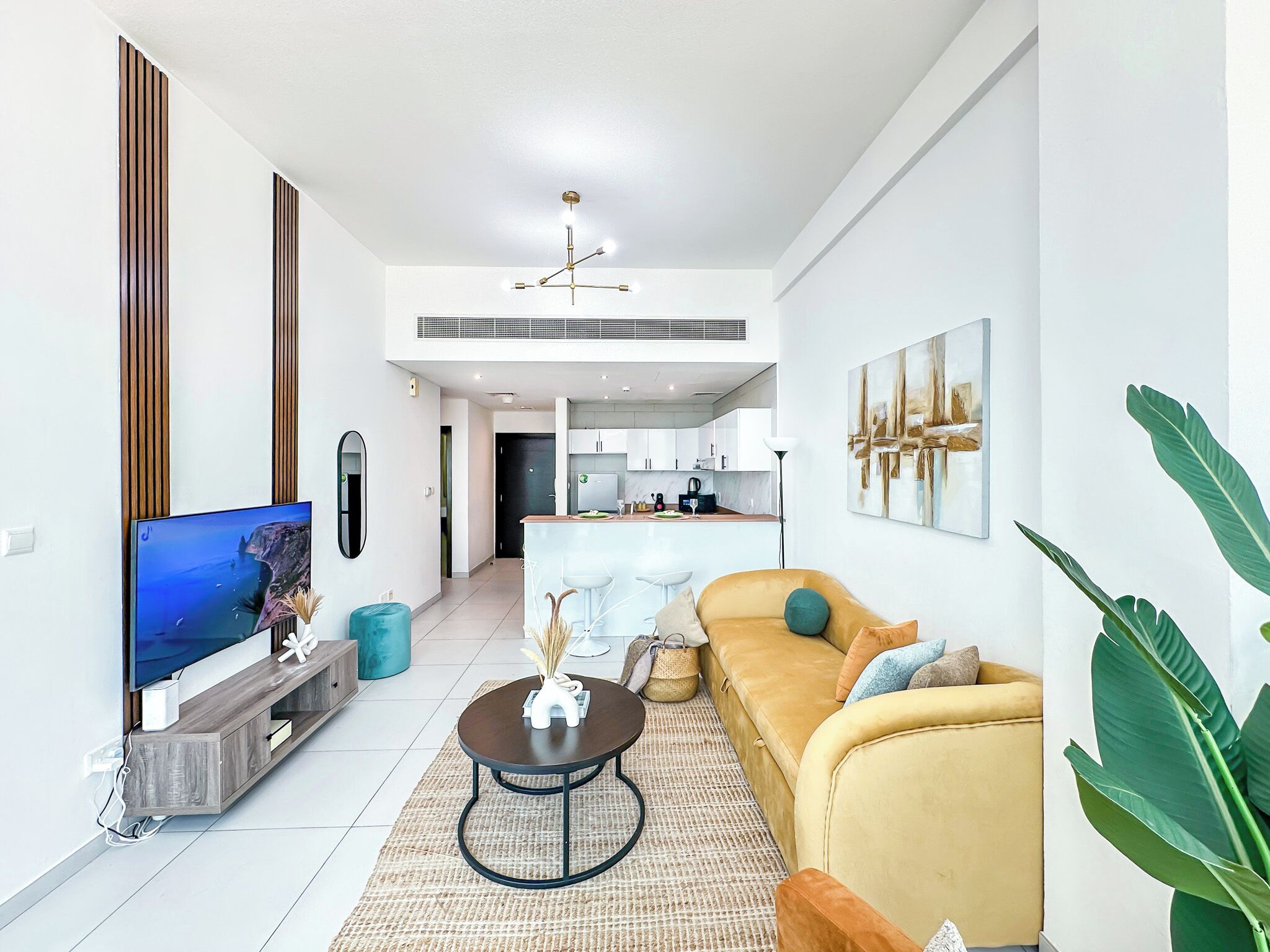 Sala de estar moderna com sofá, mesa de centro, televisão e cozinha ao fundo.