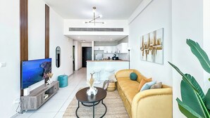 A modern living room with a sofa, coffee table, TV, and kitchen in the background. - Marina View Stay with Rooftop Pool (Dubai)
