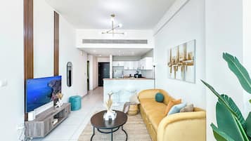 Sala de estar moderna com sofá, mesa de centro, televisão e cozinha ao fundo.