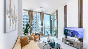 A modern living room with a sofa, coffee table, and TV. Large windows offer a view of a cityscape. - Marina View Stay with Rooftop Pool (Dubai)