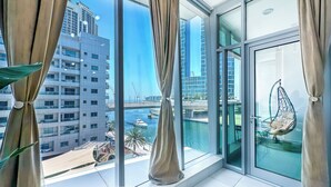 A modern room with large windows, a hanging chair, and a view of a river and buildings. - Marina View Stay with Rooftop Pool (Dubai)