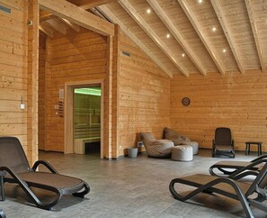 A log cabin interior with a high ceiling, wooden walls, a seating area with chairs and cushions, and a visible door leading to another room. - Doppelhaushaelfte in Hasselfelde (Hasselfelde)
